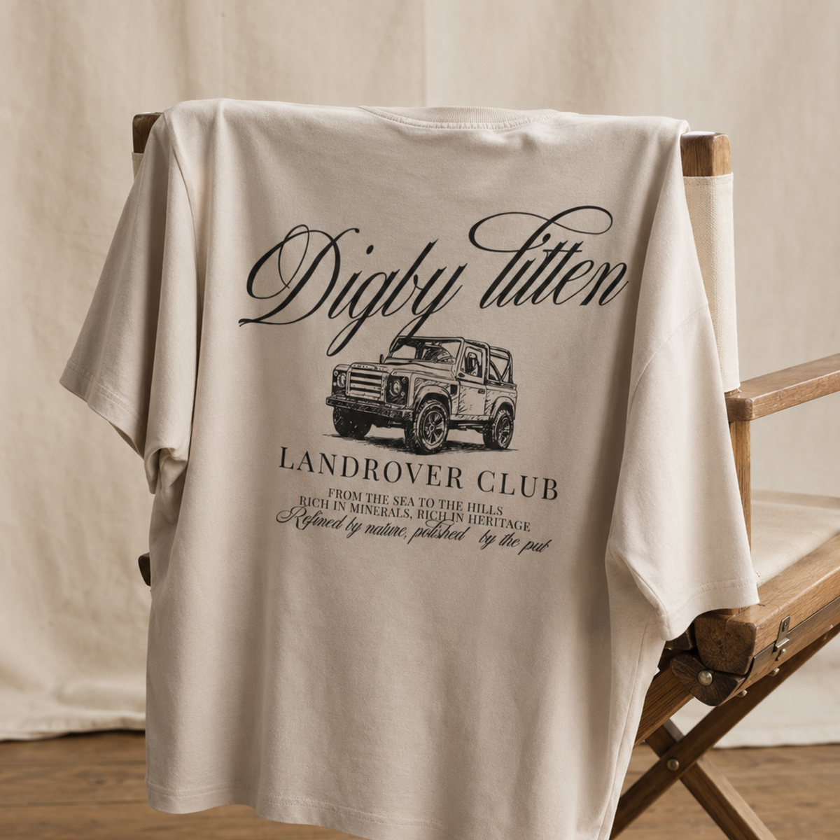 Beige Land Rover Club T-Shirt draped over a chair, showing the back graphic.