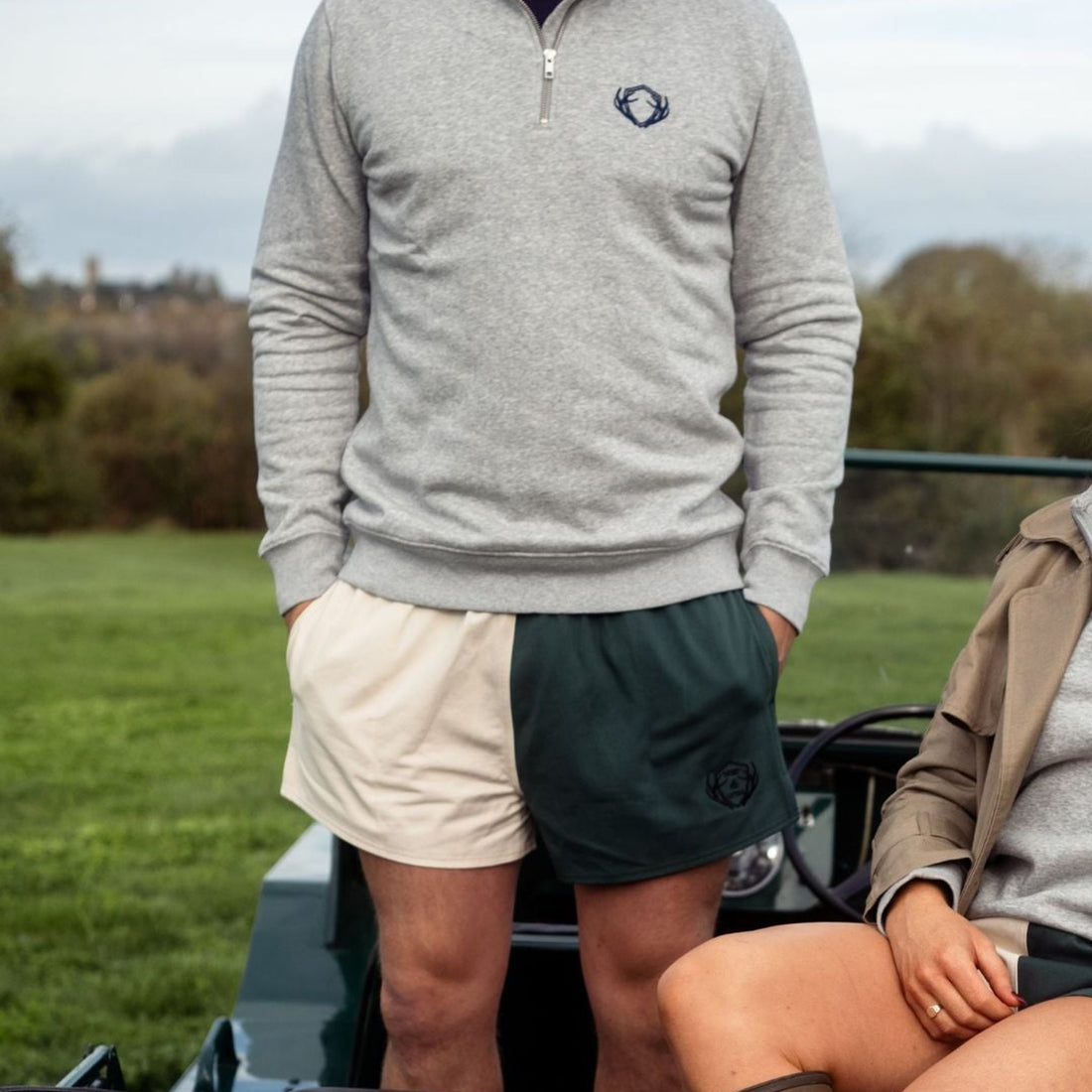 Man wearing khaki and cream Digby &amp; Litten rugby shorts with a grey quarter-zip, standing beside a vehicle.