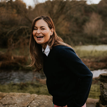 Woman wearing coral and turquoise Digby &amp; Litten rugby shorts with a dark sweater beside a stone wall.